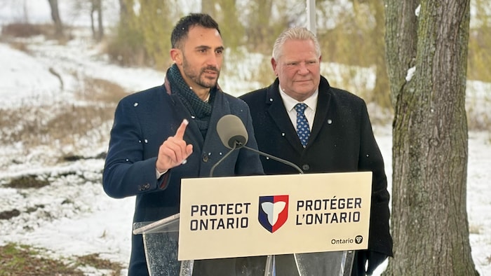 Stephen Lecce et Doug Ford sous la neige, derrière un pupitre et un micro.