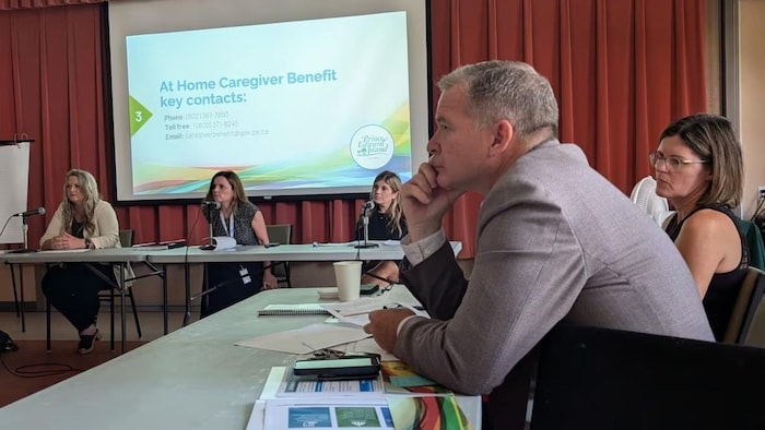 Un homme assis à une table, quatre autres personnes avec lui.