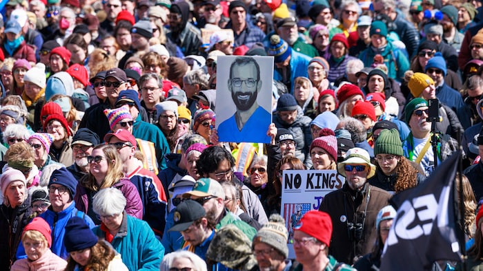 Une foule de personnes marche dans la rue, une personne brandit une pancarte montrant un homme souriant.