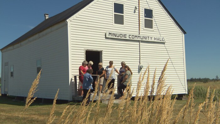 Des femmes en avant d'un édifice où il est écrit : « Minudie Community Hall »
