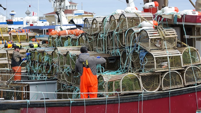 Des pêcheurs sur des bateaux remplis de casiers à homard.