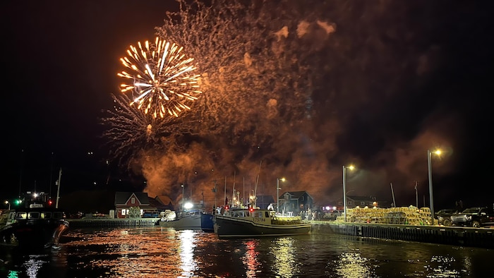 Un feu d'artifice derrière un port avec des homardiers.