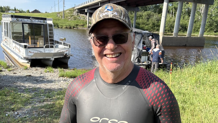 Daniel Burke pose devant des bateaux et la rivière Harricana.