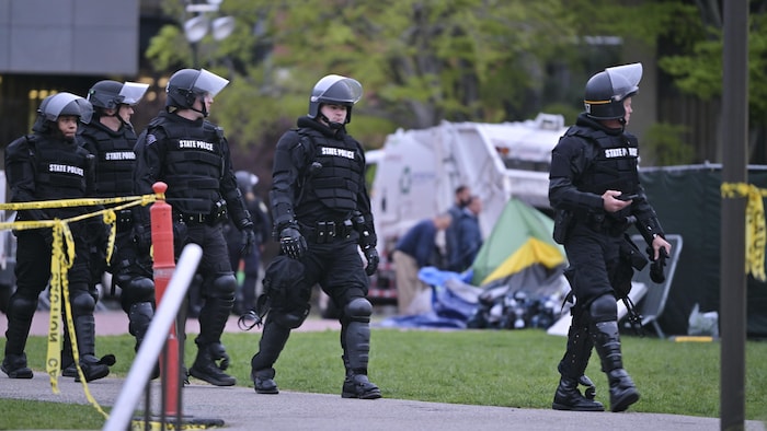 Des policiers antiémeute marchent en rang devant des tentes démontées.