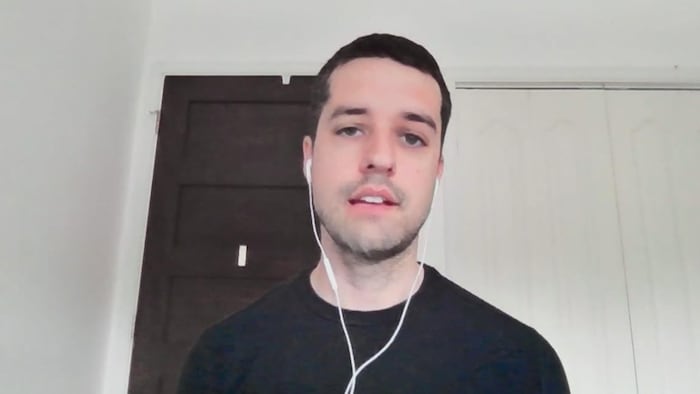 Capture d'écran d'une entrevue en visioconférence. Mitchell Dion regarde directement la caméra. Il porte des écouteurs à fils dans ses oreilles.