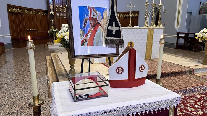 On voit une mitre, une calotte, et une photo sur une table dans une église.