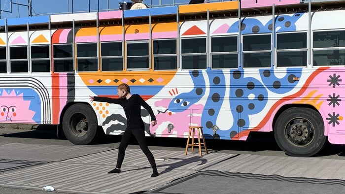 Une adolescente danse devant un autobus coloré.
