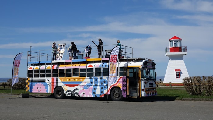 Des jeunes musiciens sur le toit d'un autobus stationné près d'un phare.