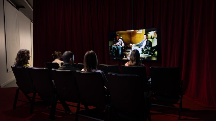 Des gens sont assis sur des chaises devant un écran où est projeté un film.