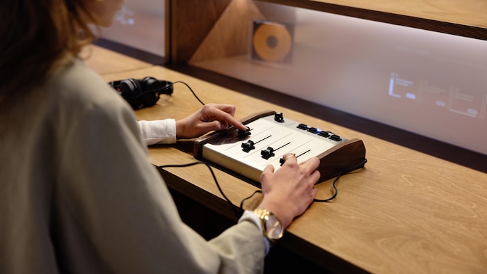 Une femme manipule une petite console de mixage, casque audio sur les oreilles.