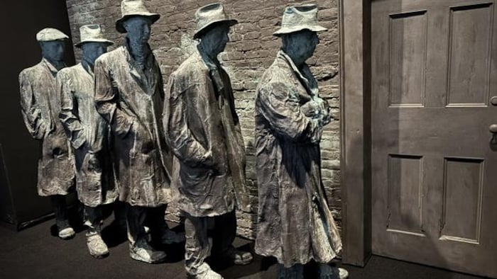 La sculpture montre cinq hommes qui attendent en ligne devant une porte.