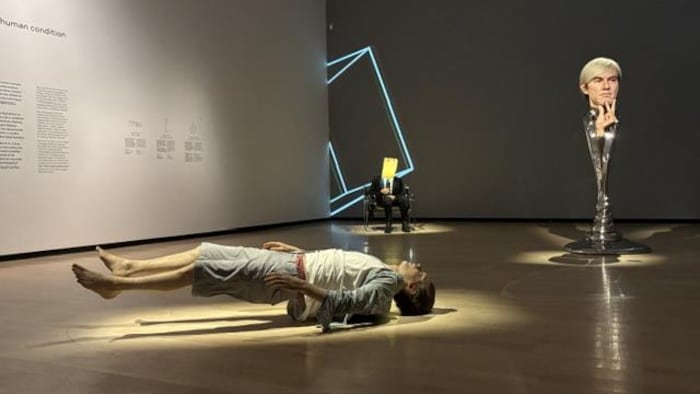 un homme qui semble tomber sur le sol, un buste et au fond, un homme assis sur une chaise avec un sac de papier sur la tête.