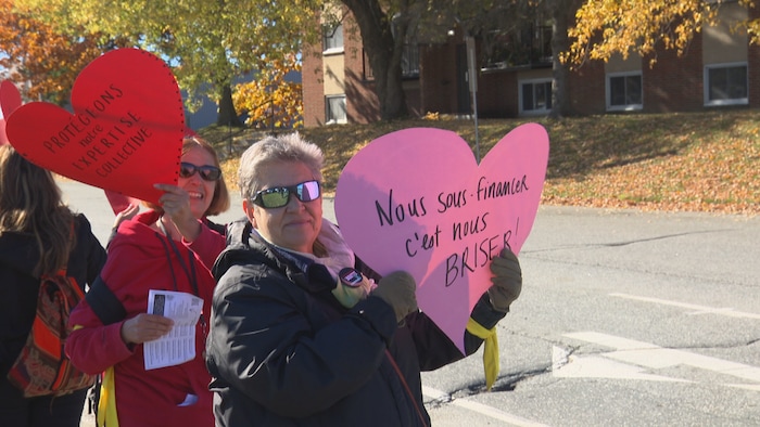 Deux dames tiennent des affiches en faveur d'un meilleur financement du milieu communautaire.