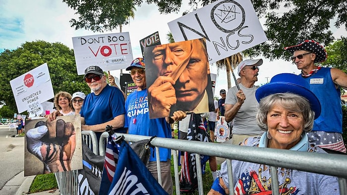 Des manifestants tiennent des pancartes, dont une montre le visage de Poutine sous celui de Donald Trump.