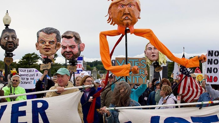 Des têtes en papier mâché représentant Donald Trump et des membres de son gouvernement tenus à bout de bras par des manifestants.