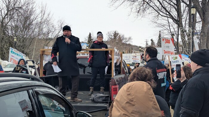 Des manifestants entourent une camionnette de type « pick-up » dans laquelle le préfet et Annie Larivière sont debout pour parler dans un micro.