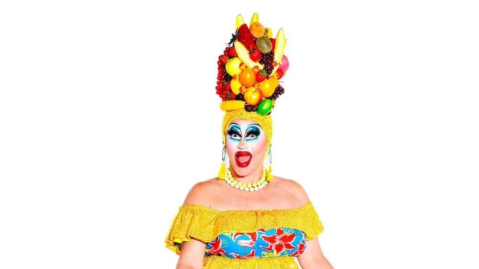 La drag queen est coiffée d'un chapeau de fruits. 
