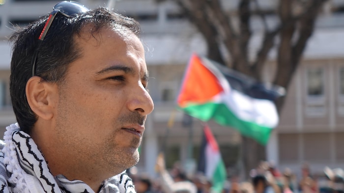 Un homme à l'avant-plan et des drapeaux palestiniens à l'arrière-plan.