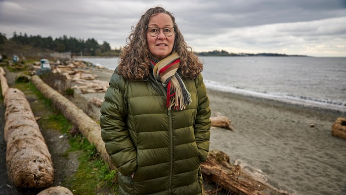 La militante libérale Moira Chambers porte un manteau d'hiver et marche sur la plage sous un ciel gris.