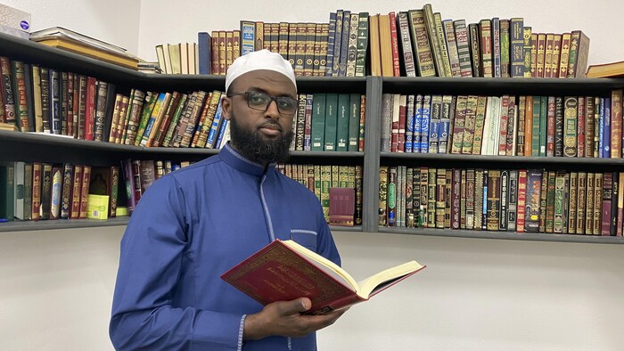 L'imam de la mosquée Sahaba au centre-ville d'Edmonton, Abdishakour Mohamed, tient un livre en main. On aperçoit de nombreux livres derrière lui.