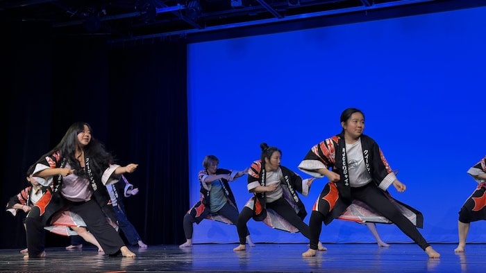 Des jeunes vêtus de vestes traditionnelles exécutent une danse rythmée sur scène lors des festivités.