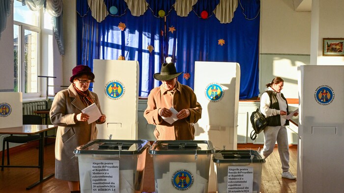 Un homme et une femme portant un manteau de laine placent leur bulletin de vote dans une boîte à la sortie d'un isoloir.