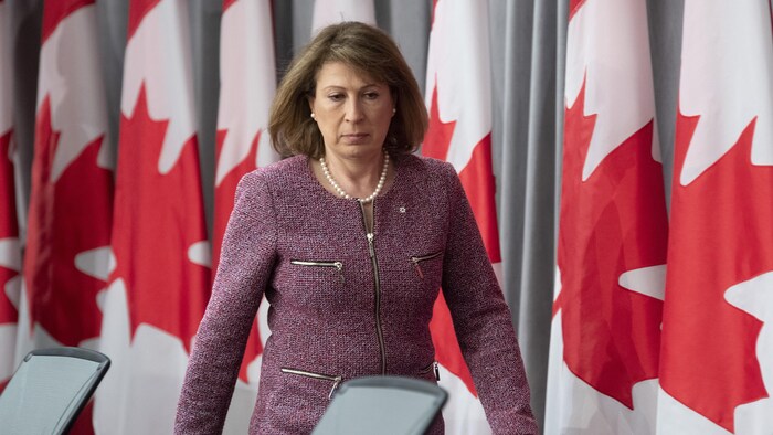 Mona Nemer marche devant des drapeaux du Canada.