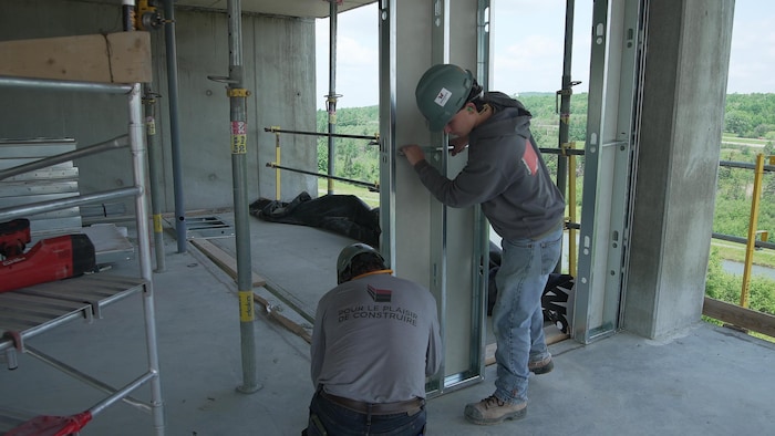 Two workers install a wall on a site.