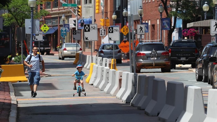 Un enfant marche à côté de son petit garçon en vélo pour enfants, le long d'une série de blocs de béton.