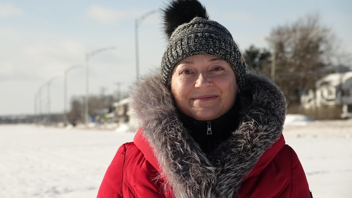 Une femme souriante porte une tenue d'hiver et une tuque, devant un paysage enneigé, Maria.