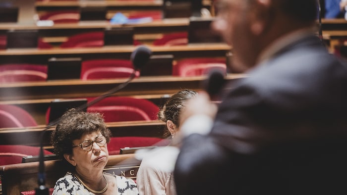 Dans une assemblée, une femme assise grimace.