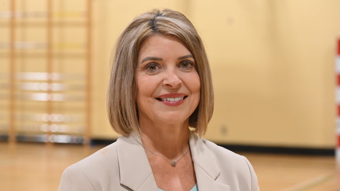 Une personne aux cheveux blonds sourit en regardant la caméra.