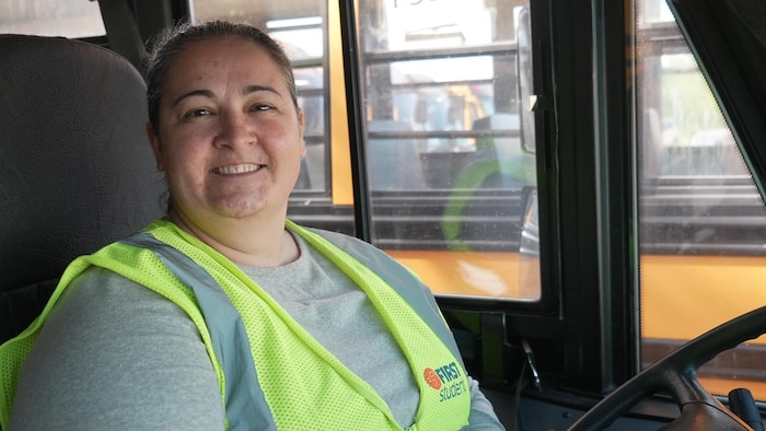 Une femme est assise derrière le volant de son autobus. 