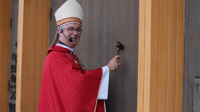 Monseigneur Pierre-Olivier Tremblay frappe sur la porte de la cathédrale avec un maillet.