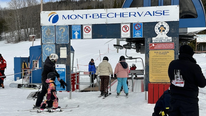 Le panneau du Mont-Bechervaise devant la remontée mécanique du centre de ski, avec des skieurs qui s'y avancent.