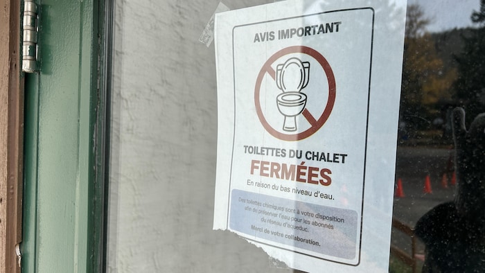 Une affiche disposée dans la fenêtre du Mont-Comi informe que les toilettes du chalet sont fermées en raison du bas niveau d'eau.