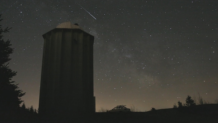 Observatório à noite com uma estrela cadente no céu estrelado.