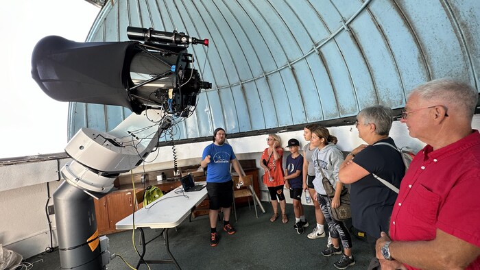 Um grupo de pessoas dentro de um observatório sob uma cúpula azul perto de um telescópio.