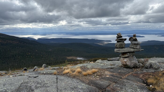 Vue sur le réservoir Manicouagan depuis le sommet du mont Provencher. À l'avant-plan, un inukchuk en pierre. En contre-bas, la forêt boréale et des îles.