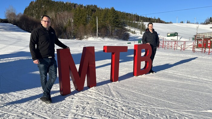 Martin Dionne et Adam Gagnon se trouvent de part et d'autre des lettres MTB sur les pistes damées du Mont Ti-Basse.