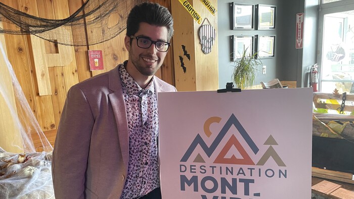 Fabien Garant sourit à la caméra près d'une affiche indiquant Destination Mont-Vidéo.