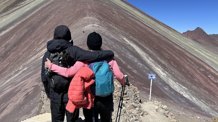 Deux personnes de dos admirent une montagne colorée.