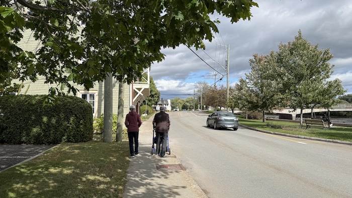 Deux personnes marchent dans la rue, dont une avec un déambulateur.
