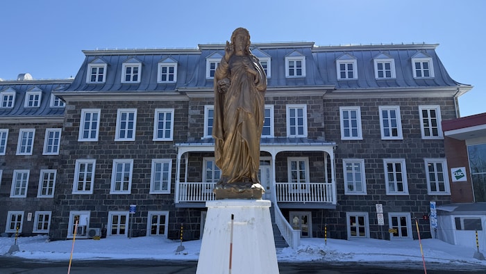 Une statue devant une bâtisse en pierres grises de quatre étages.