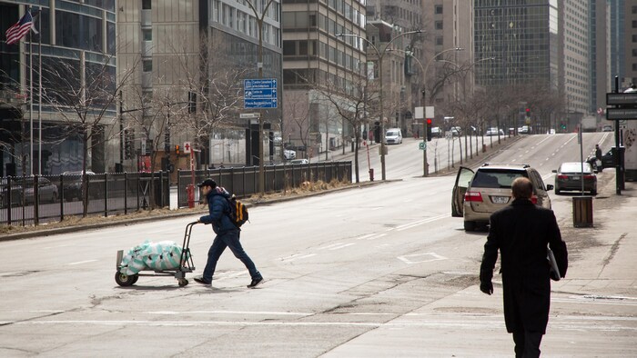 Un homme traverse la rue en poussant un chariot de marchandise.