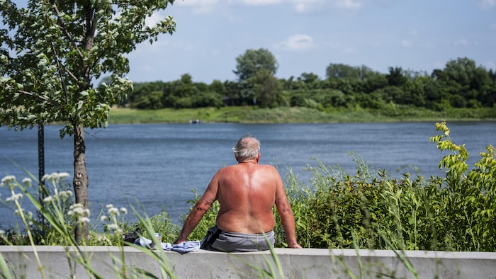 Un homme, le dos rougi par le soleil, est assis sur le bord de l'eau à Montréal.