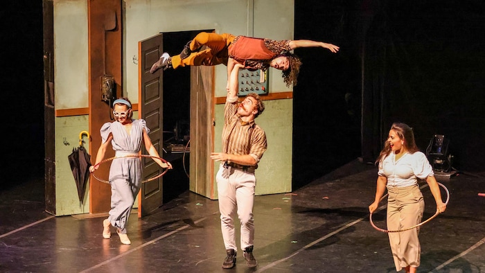 Un artiste de cirque en tient un autre en équilibre sur sa main dans les airs, avec deux artistes autour. 