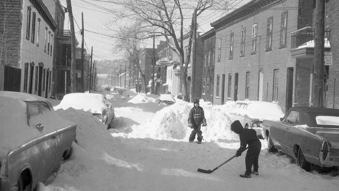 Deux enfants jouent au hockey dans la rue.