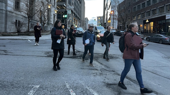 Une demi-douzaine de personnes marchent dans une rue du centre-ville à la tombée du jour.