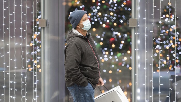 Un homme masqué marche devant un commerce illuminé.
